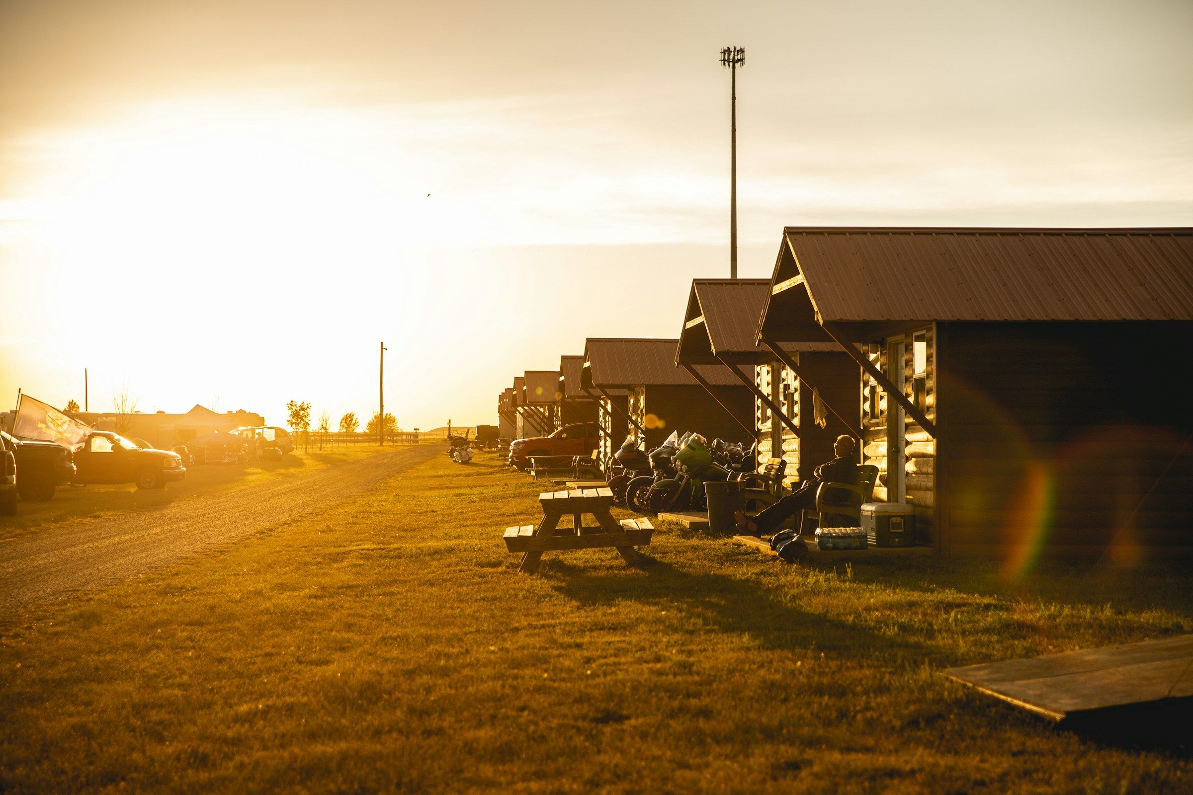 A row of log bunkhouse cabins with picnic tables at golden hour
