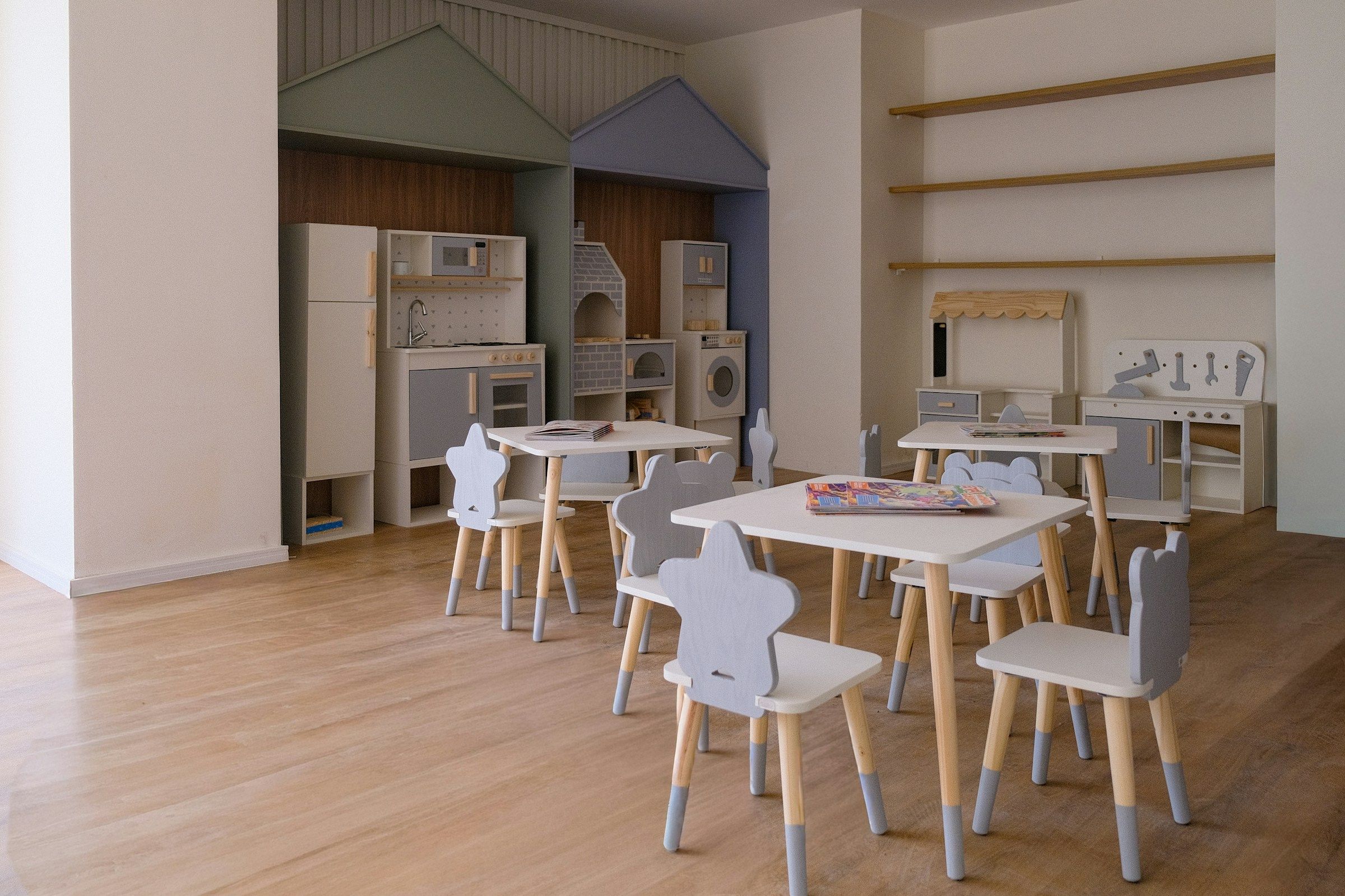 An empty daycare playroom with low tables, small chairs and play kitchens