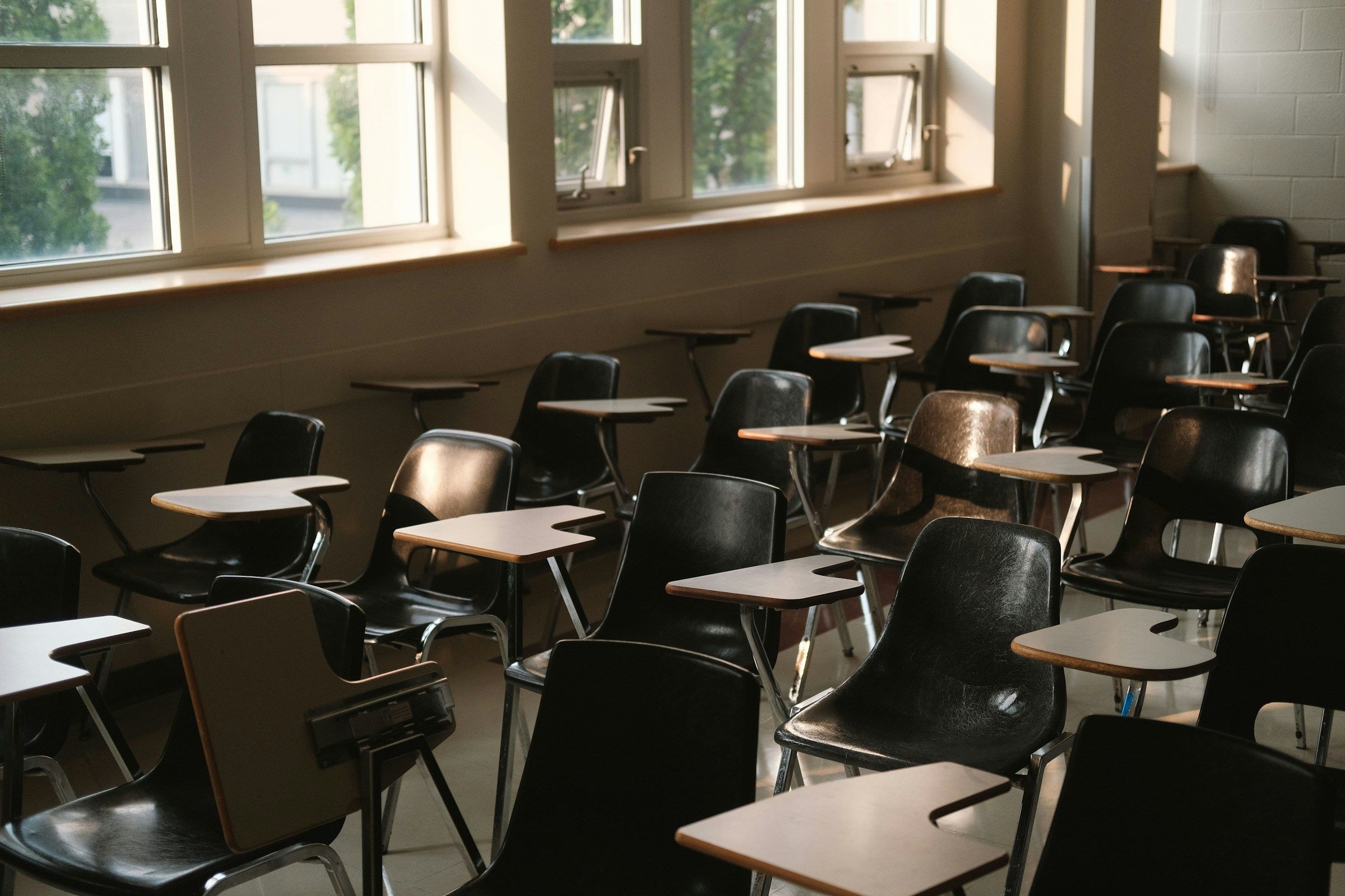 An empty classroom with tablet-arm desks beside a row of open windows